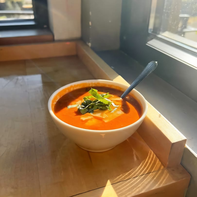 A bowl of Versalia Pizza's tomato soup with basil and cheese, bathed in sunlight.