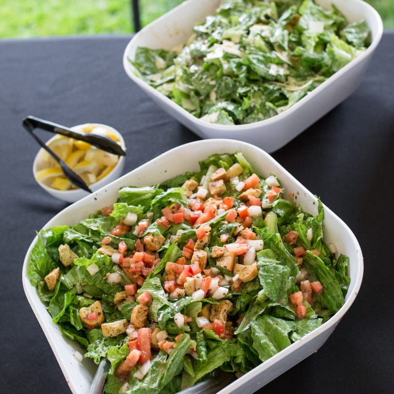 Two large white bowls of fresh green salad with tomatoes, croutons, and dressing on a black tablecloth.