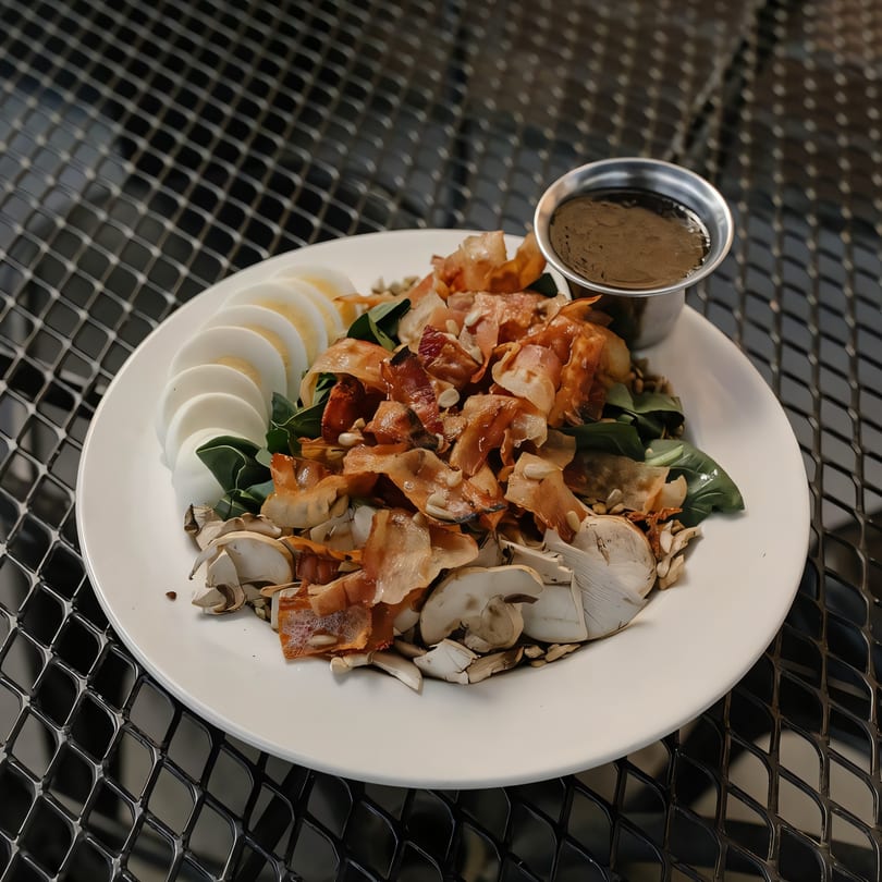 A Versalia Pizza salad with sliced hard-boiled eggs, mushrooms, greens, and a side of dressing.