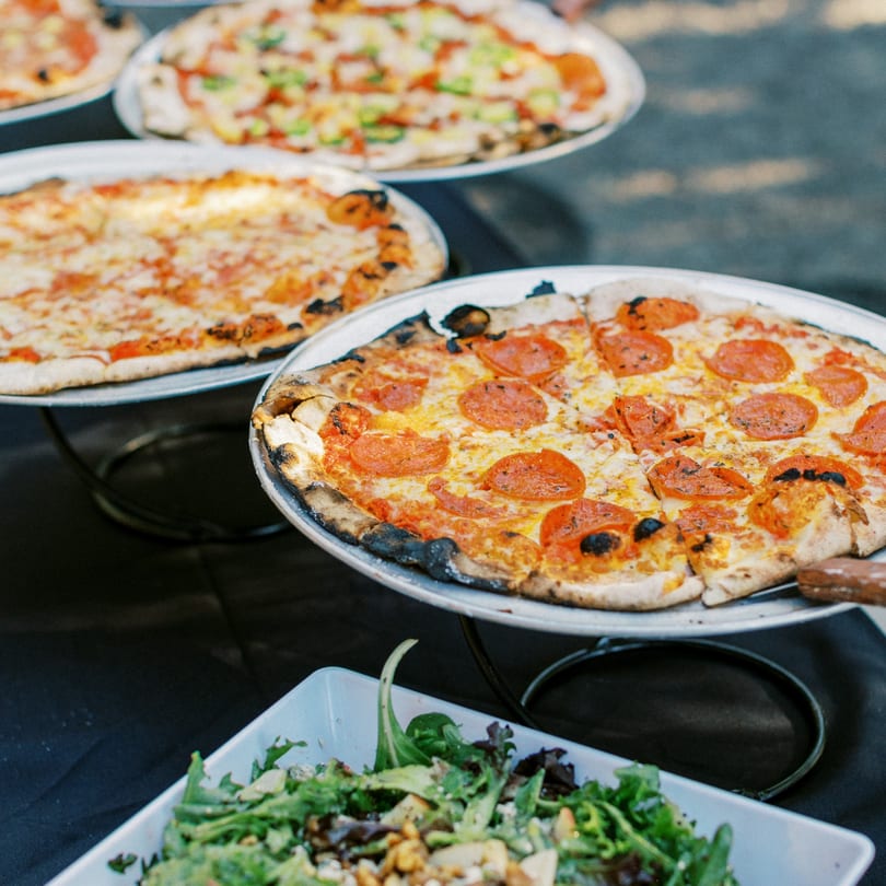 Multiple Versalia pizzas, including pepperoni and cheese, on stands with a salad in the foreground.