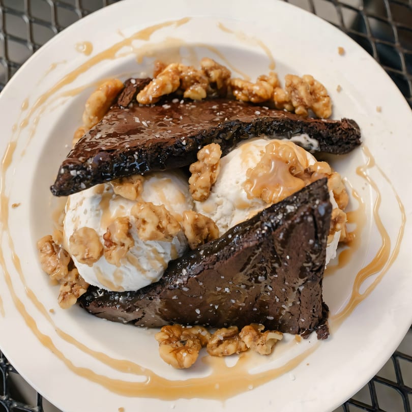 Versalia Pizza's brownie dessert with vanilla ice cream, walnuts, and caramel drizzle on a white plate.