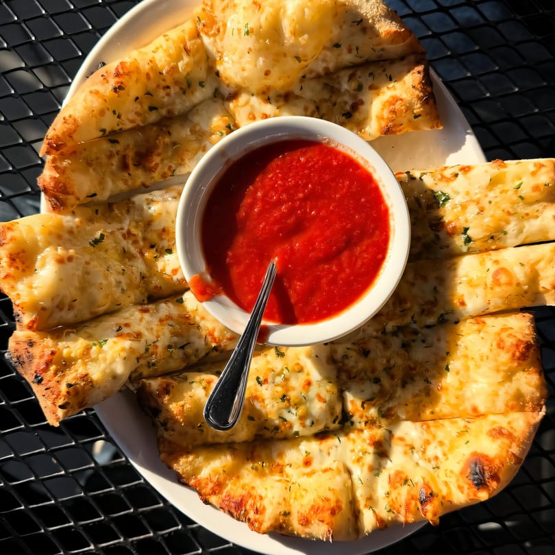Cheesy garlic breadsticks with herbs and a side of red marinara sauce on a white plate.