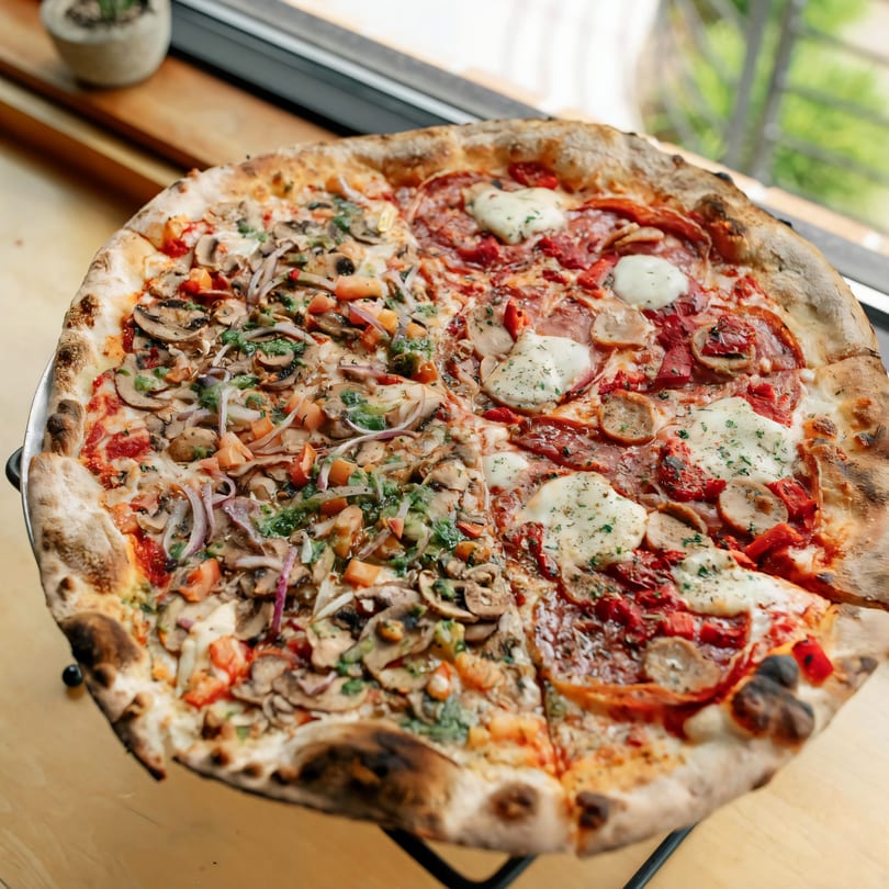 A large Versalia Pizza with two different halves, one with mushrooms and vegetables, the other with pepperoni and sausage.